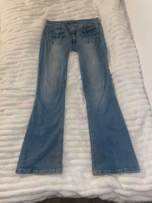 Blå utsvängda jeans från Lipp - Säljer ett par ljusblå jeans från Lipp med utsvängda ben och snygga fickdetaljer framtill. Jeansen har låg midja och klassisk femficksdesign. Perfekta för dig som gillar retrostil och vill ha ett par unika jeans i garderoben.