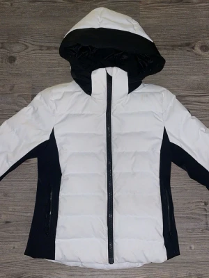 Jacka Everest - Snygg Skidjacka från Everest i vitt med svarta detaljer och huva. Perfekt för kalla vinterdagar. Har använt som både skidjacka och vanligt ”vardagsbruk”. Använd fåtal gånger 💕💕Storlek 34. Nyskick pris 3000 :-.
