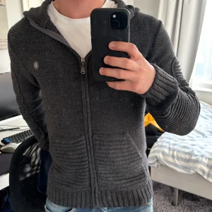 Paddock's stickad kofta  - Mörkgrå stickad kofta från Paddock’s. Nyskick, inga tecken alls på användning. Gjord i 100% Akryl vilket gör den bra på att behålla värme. Skriv gärna om du har funderingar!