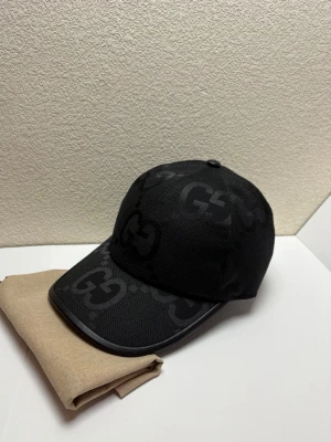 Svart GG keps - Snygg svart keps med det klassiska GG-logomönstret över hela kepsen. Kepsen har böjd skärm och är tillverkad i ett slitstarkt tygmaterial som ger en exklusiv känsla. Perfekt för dig som vill ha en trendig accessoar med lyxig vibe.