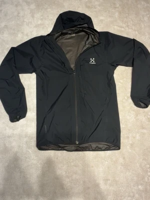 Svart regnjacka från Haglöfs, S - Säljer en svart regnjacka från Haglöfs i storlek S. Jackan har huva, hel dragkedja framtill och diskret Haglöfs-logga på bröstet.. Använd fåtal gånger och är i bra skick.                                                     Pris kan dissekeras vid snabb affär 