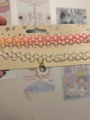 Chokerhalsband i plast med berlock - Säljer ett set med två chokerhalsband i plast. Ett är i regnbågsfärger, ett i vitt med en liten rund berlock med strass. Perfekt för dig som gillar Y2K-stil och vill ha något färgglatt och lekfullt till din outfit. <3