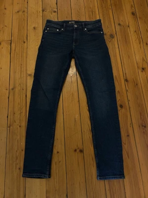 Mörkblå jeans från Only & Sons - Säljer ett par mörkblå jeans från Only & Sons med klassisk femficksdesign och raka ben. Jeansen har silverfärgade nitar och knapp, samt bälteshällor. Materialet är slitstark denim i bomull. Perfekta för en avslappnad och stilren look.