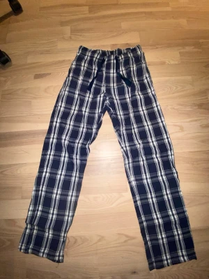 Rutiga pyjamasbyxor i blått och vitt - Säljer ett par klassiska pyjamasbyxor med blå och vit rutig design. Perfekta för chillkvällar hemma. 