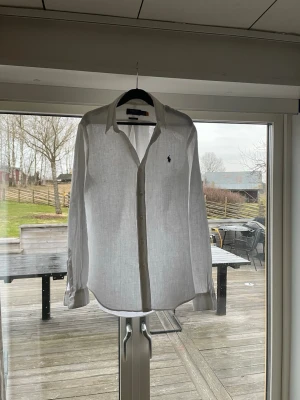 Vit linneskjorta från Polo Ralph Lauren - Riktigt fräsch Ralph lauren linneskjorta som är i bra skick. Storleken är small men skulle ändra säga att den passar runt medium med. Den har inga defekter och är perfekt nu till våren och sommaren, hör av er vid frågor eller funderingar!