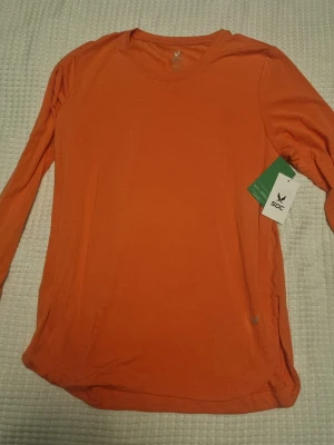 Långärmad tröja från SOC - Aprikos/orange långärmad topp från SOC med rund halsringning. Tillverkad i ett mjukt och lätt material som känns skönt mot huden. Perfekt att bära som lager eller för en enkel och clean look. Oanvänd och taggen kvar.