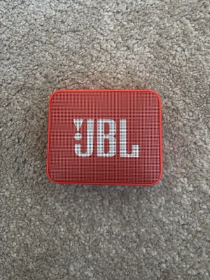 Röd JBL Go bärbar högtalare - Oandvänd snygg och kompakt röd JBL Go bärbar högtalare med tydlig JBL-logga på framsidan. Högtalaren har en rektangulär form och är tillverkad i plast med ett metallgaller framtill. Perfekt för att ta med sig överallt och spela musik trådlöst. OBS- morsan slängde paketet på den så den kommer utan original förpackning😢 