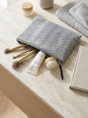 Grå sminkväska i mjukt tyg - Snygg grå sminkväska med fiskbensmönster och dragkedja. Väskan är tillverkad i ett mjukt tygmaterial och har en stilren, rektangulär form. Perfekt för att förvara sminkborstar och andra småsaker. Enkel att ta med i väskan eller ha på sminkbordet.