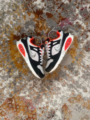 Nike Air Max 200 svart/vit/röd - Nike Air Max 200 sneakers i svart, vitt och rött med silverfärgad Swoosh. Ovandelen är i mesh och syntet, med tydliga Air Max-detaljer och synlig luftbubbla i sulan. Skorna har vita snören och röda detaljer runt häl och plös.