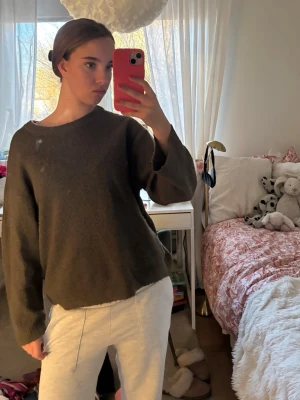 Olivgrön stickad tröja från 157 - Mysig olivgrön stickad tröja från 157 med rund halsringning och avslappnad passform. Tröjan har långa ärmar och är gjord i ett mjukt, fluffigt material som känns skönt mot huden. Perfekt för lager på lager under kyliga dagar.