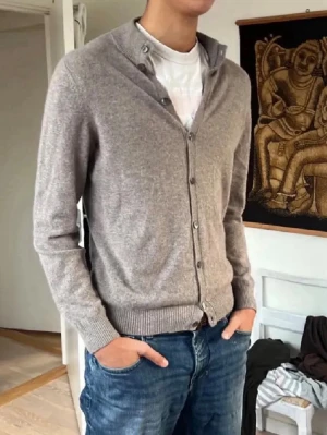 Stenströms Cardigan  - Snygg gråmelerad kofta från Stenströms med knäppning framtill och ribbade muddar. Klassisk passform och mjukt material som känns skönt mot huden. Perfekt att slänga över en t-shirt för en avslappnad look. 100% Kashmir 