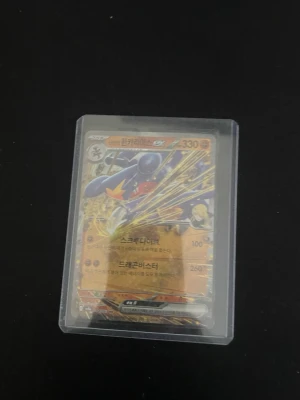 Pokémonkort i plastficka - Unikt Pokémonkort med färgstark design och holografiska detaljer, förvarat i genomskinlig plastficka. Kortet har motiv med figurer och text på koreanska samt en baksida med neonrosa och gröna illustrationer. Perfekt för samlare eller Pokémonfans.