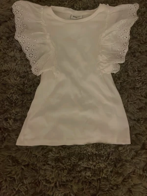 Vit topp med volangärmar och spets - Söt vit topp  med volangärmar i broderad spets. Toppen har en rak passform och är tillverkad i mjukt bomullstyg. Knappt använd