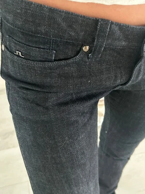 Mörkblå bootcut jeans från JL - Snygga mörkblå bootcut jeans från J.Lindeberg med klassisk femficksmodell och silverfärgade nitar. Jeansen har en diskret JL-logga på myntfickan och är tillverkade i ett stretchigt denimtyg som sitter tajt upptill och släpper ut vid bensluten.