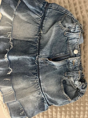Blå jeanskjol med volanger - Säljer en kort jeanskjol i blå denim med   volangdetaljer. Perfekt för sommaren! Pris går att diskuteras