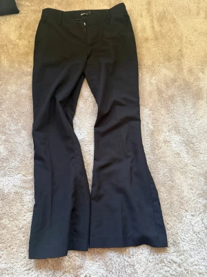 Svarta utsvängda kostymbyxor - Säljer ett par svarta kostymbyxor med utsvängda ben och låg midja från Gina. Strl 36 i petite 