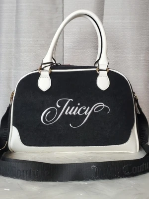Juicy Couture svart och vit handväska - Snygg svart och vit handväska från Juicy Couture med broderad logga framtill. Väskan har både handtag och justerbar axelrem, detaljer i vitt konstläder och guldiga metalldelar. Perfekt för dig som gillar en trendig och sportig look.