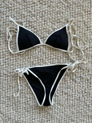 Ny! Svart och vit bikini från H&M Stl 36 - Snygg svart bikini från H&M med vita kanter och tunna knytband både upptill och nedtill. Klassisk trekantsmodell som ger en stilren look på stranden. Perfekt för sommaren och enkel att matcha med andra plagg.