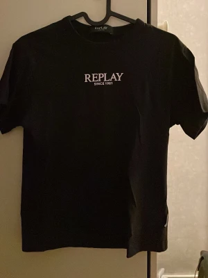 Svart t-shirt från Replay - Svart t-shirt från Replay med vit logga och texten 'SINCE 1981' på bröstet. Klassisk rund halsringning och korta ärmar. Perfekt basplagg med stilren design som funkar till det mesta.