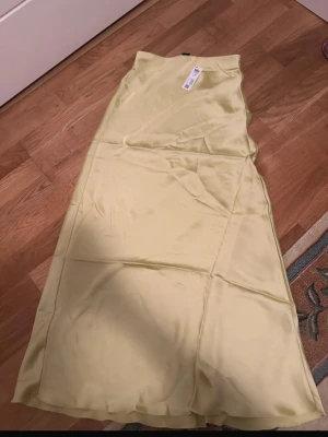Ljusgul satinkjol från Lindex stl xs - Supersnygg långkjol i ljusgul satin från Lindex Kjolen har en slät och glansig yta som ger en lyxig känsla och är perfekt för dig som gillar en stilren look. Enkel design utan mönster och med en lätt utställd form.