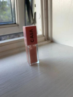 CAIA ljusrosa läppglans - Säljer ett läppglans från CAIA i en snygg ljusrosa nyans. Förpackningen är fyrkantig med en rosa kork och transparent kropp som visar färgen. Perfekt för dig som vill ha glansiga och mjuka läppar med en hint av färg. Endast testad 