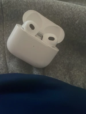 Vita trådlösa hörlurar Apple AirPods - Säljer ett par vita trådlösa hörlurar Apple AirPods med laddningsetui. Hörlurarna har en stilren och kompakt design i blank plast och passar perfekt för musik, poddar och samtal. Smidig laddning direkt i etuiet och enkel anslutning till din mobil.