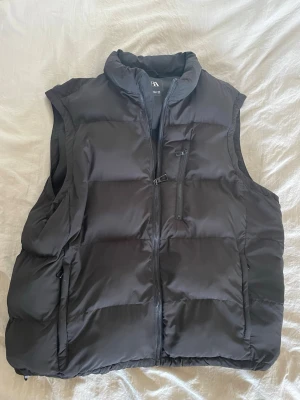 Svart dunväst från Zara - Svart dunväst från Zara med hög krage och dragkedja framtill. Västen har två sidofickor med dragkedja och en bröstficka med dragkedja. Klassisk puffer-modell som är perfekt för lager-på-lager-stil. 