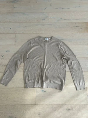 Beige rundhalsad tröja från Bläck - Stilren beige tröja med rund halsringning och långa ärmar. Tillverkad i en mjuk ullblandning som känns skön mot huden. Perfekt för lager-på-lager och enkel att matcha med olika outfits.