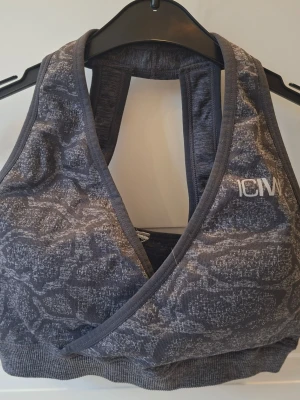 Grå sport-bh från ICANIWILL. Seamless sports bra graphite - Sport-bh i grått med mönstrad design och omlottfront från ICANIWILL. Bh:n har bred resår nedtill, dubbla axelband bak och är tillverkad i ett stretchigt funktionsmaterial som andas. Perfekt för träning och aktiva dagar.