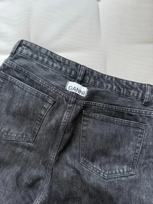 Svarta raka jeans från Ganni - Säljer ett par svarta jeans från Ganni med rak passform och klassisk femficksdesign. Jeansen har dragkedjegylf och knapp, samt bälteshällor i midjan. Materialet är kraftig denim i svart färg.