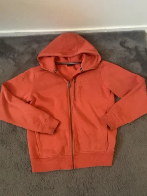 Orange hoodie med zip från Sail Racing - Säljer en röd hoodie från Sail Racing med dragkedja. Den är nästan helt ny. Har använt 4 gånger och den är för liten.
