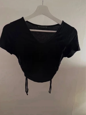 Svart croppad topp med snörning PrettyLittleThing - Svart croppad topp från PrettyLittleThing med v-ringning och snörning framtill. 
