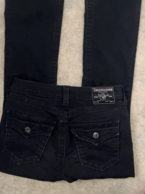 Svarta jeans från True Religion - Snygga svarta jeans från True Religion med klassiska fickor bak och tydliga sömmar. Jeansen har en patch med logga på bakfickan och coola knappar på ficklocken. Säljer pga de är för långa på mig och är 164cm lång
