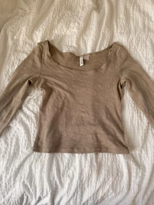 Två långärmade toppar från H&M - Säljer två stilrena långärmade toppar från H&M, en i beige och en i vit. Båda har en bred, rundad urringning och är tillverkade i mjuk bomullsmix. Perfekta att matcha med jeans eller kjol för en enkel och snygg look.