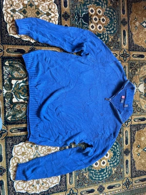 Blå stickad tröja från Chaps - Snygg blå stickad tröja från Chaps med halv dragkedja och ribbad krage. Tröjan har långa ärmar, ribbade muddar och diskret broderad logga på bröstet. Perfekt för dig som gillar klassisk och enkel stil.