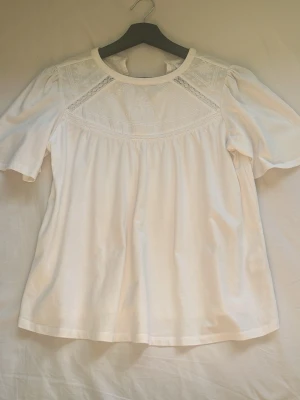 Vit blus med spets från Zara - Superfin vit blus från Zara med broderade detaljer och spets upptill. Blusen har korta ärmar och rund halsringning, perfekt för en fräsch och stilren look. Tillverkad i mjuk bomull som känns skön mot huden.