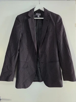 Svart kavaj med smala ränder H&M - Snygg svart kavaj från H&M med tunna vita ränder. Klassisk modell med två fickor framtill och en bröstficka. Tunn, fodrad insida och smal passform. Perfekt för en stilren look.