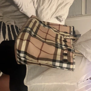 Rutig shoppingväska från Burberry - Säljer en klassisk shoppingväska från Burberry med det ikoniska rutiga mönstret i beige, brunt, svart och vitt. Väskan har grova rep-handtag och metallögla-detaljer upptill. Perfekt storlek för att få plats med allt du behöver och riktigt snygg att bära på axeln.