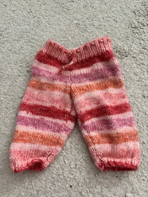 Randiga stickade byxor i rosa toner för dockor - Säljer ett par handstickade byxor med breda ränder i rosa, rött, orange och vitt för dockor. De har resår i midjan och är gjorda i mjukt garn, perfekta för dockor!