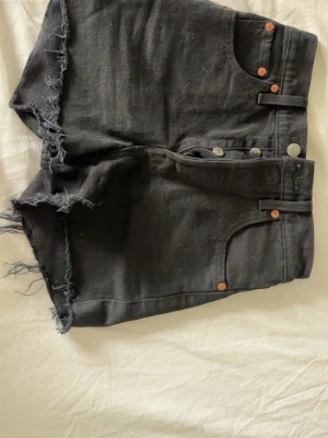 Svarta jeansshorts från Levi's - Svarta jeansshorts från Levi’s. De är hela och inga defekter. Det är storlek 23 och de sitter tajt på mig som vanligtvis har xs. Dem är väldigt tighta i midjan så jag får inte knäppt dem. Så jag skulle tro att de passar någon som har tex xxs eller en större barn storlek så som 146-157. 