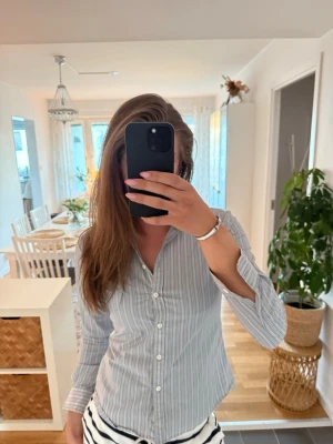 Gråvit randig skjorta med smal passform - Snygg skjorta i grått med tunna vita ränder och klassisk krage. Skjortan har lång ärm, knäppning framtill och figurnära passform. Perfekt för en stilren look och passar till både jeans och kostymbyxor.