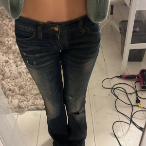 Mörkblå bootcut jeans med slitningar - Säljer ett par mörkblå jeans med bootcut-modell och snygga slitningar på knäet. Jeansen har klassisk femficksdesign, låg midja och är tillverkade i jeansmaterial. Perfekta för dig som gillar en avslappnad och trendig look.