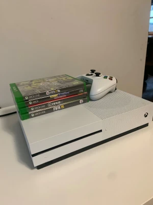 Xbox One S med handkontroll och spel - Säljer en vit Xbox One S med en matchande vit trådlös handkontroll. Konsolen har en stilren, rektangulär design i plast och kommer med flera spel, bland annat FIFA och Sonic. Perfekt för gamingkvällar och multiplayer med vänner.