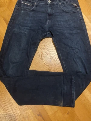Mörkblå jeans från Replay - Snygga mörkblå jeans från Replay med klassisk femficksdesign och raka ben. Jeansen har en diskret tvättad look och silverfärgad knapp med Replay-logga. Perfekta för dig som gillar stilrena och tidlösa jeans.
