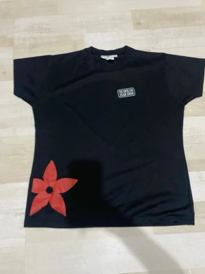 Svart t-shirt Tjejmilen 2008 - Svart t-shirt från Jingham med trycket 'Tjejmilen 25 år 2008' på bröstet och en stor röd blomma nertill. Klassisk rund hals och korta ärmar. Perfekt för dig som gillar unika sportiga plagg med cool detalj.