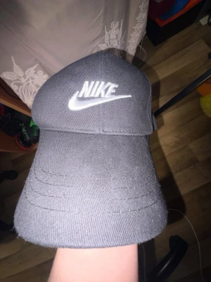 Svart Nike keps med broderad logga - Snygg svart keps från Nike med klassisk böjd skärm och vit broderad logga framtill. Kepsen är i bomullstyg och har en stilren, sportig look som passar till det mesta. Justerbar baktill för perfekt passform.
