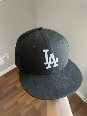 Svart LA-keps från New Era - Snygg svart keps från New Era med LA-Dodgers logga broderad framtill i vitt. Jag har bara använt kepsen mer än 5 gånger sedan jag köpte den i höstas. Modellen är 9FIFTY och kepsen är tillverkad i 100% bomull. Perfekt för dig som är snygg.