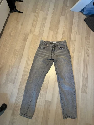 Ljusblå grå med svart aktig färg - Säljer ett par ljusgrå med lite svart med rak passform och klassisk femficksdesign. Jeansen har normal midja och är tillverkade i denim. Perfekta för en avslappnad och trendig look. Midjan har storlek 27 och längnd 30