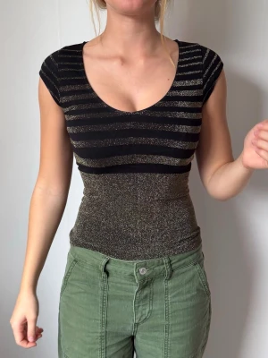 Svart och guld glittrig topp - Snygg svart topp med glittriga guldränder och tight passform. Köpt secondhand men står i etiketten att märket är Guess Jeans