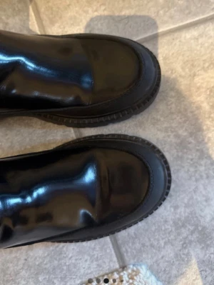 Svarta GANT boots  - Snygga svarta GANT boots i glansigt skinn från GANT. Klassisk rund tå, bred resår på sidorna och grov sula för en cool look. Perfekta till både jeans och kjol för en trendig stil.
